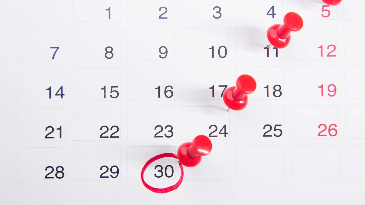 Calendário de parede com alfinetes vermelhos espetados em dias espaçados do mês e o dia 30 circulado à caneta