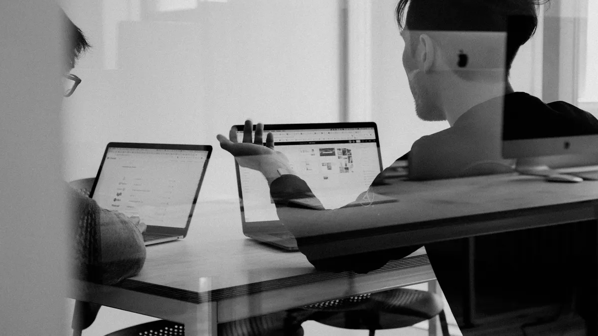 Duas pessoas em uma reunião, cada uma com um notebook aberto, em foto preto e branco